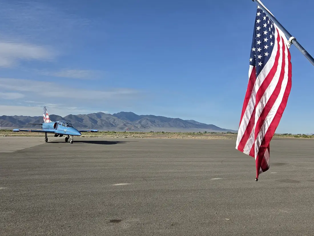 An American flag and a trainer jet on the ramp at Battle Mountain Airport, mountains in the background